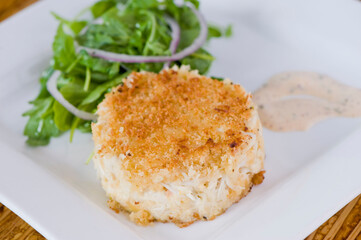 Crab cake. Crab served with spicy rémoulade sauce on top of a mixed green salad. Jumbo crab meat mixed with garlic, onions, spices & fried in butter. Classic American restaurant appetizer.