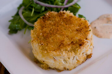 Crab cake. Crab served with spicy rémoulade sauce on top of a mixed green salad. Jumbo crab meat mixed with garlic, onions, spices & fried in butter. Classic American restaurant appetizer.