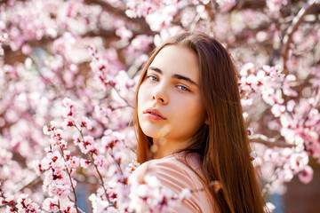 Young girl posing near blossom cherry tree with pink flowers