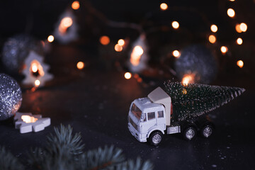 Toy truck with a Christmas tree on a dark background . Christmas concept. Bokeh garland