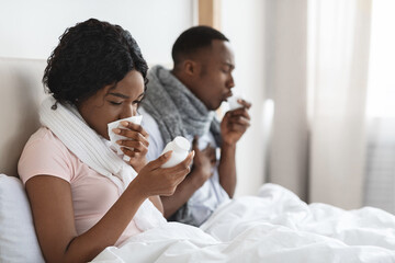 Sick couple sitting in bed, coughing and sneezing