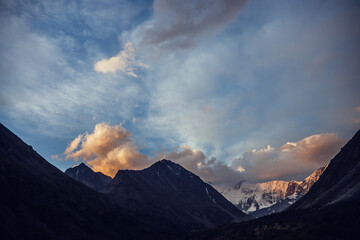 Amazing vivid landscape of sunset with awesome mountain silhouettes and orange clouds. Atmospheric highland scenery with great silhouettes of mountains under dawn sky. Snowy mountains in orange clouds