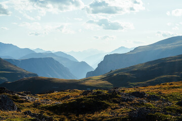Fototapeta premium Scenic mountain landscape with giant rockies and deep gorge behind green hill in sunlight. Wonderful vivid sunny highland scenery with big rocks and precipice. Awesome view to great mountains.