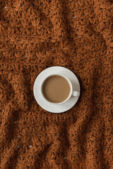 Flatlay cup of coffee on brown crumpled knitted traditional woolen textile cloth texture. Fashion pattern. Flat lay, top view.