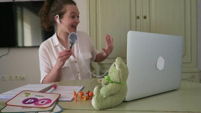 Young, attractive woman teaching English online to children. Singing ABC's with her students, using teaching props. Lesson, education, professional.