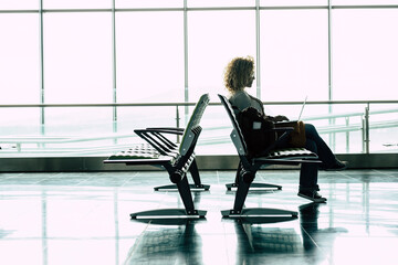 Travel and work online job people at the airport gate - woman sit down and wait for her flight with laptop computer in smart working or digital nomad free lifestyle alternative