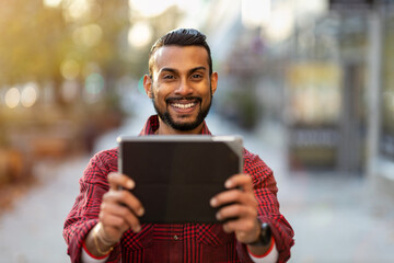 Smiling young man using tablet outdoors at urban setting
