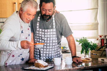 Couple of adult and senior man father and son or friends  bake together at home in the kitchen having fun - baking activity at home with different ages people