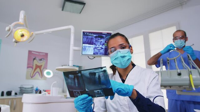 Patient pov in dental office planning surgery steps of teeth cavity, dentist pointing on x-ray image. Stomatology doctor wearing protective mask and gloves, working in modern stomatological clinic