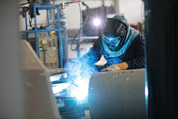 Speicalist welder wearing PPE welding piping and construction structure, steel weld spark from arc welding