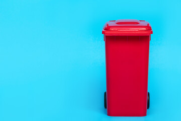 red wheelie waste bin on blue background.
