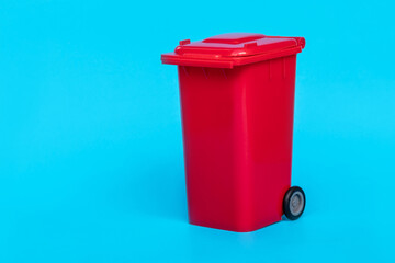 red wheelie waste bin on blue background.