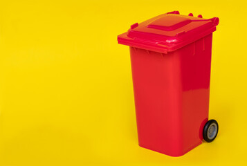 red wheelie waste bin on yellow background.