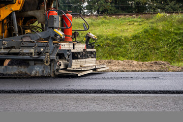 Industrial asphalt paver machine laying fresh asphalt on road construction site.