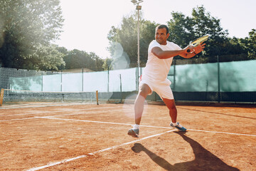 Fit man plays tennis on tennis field