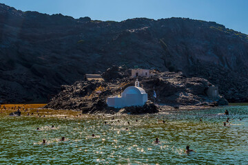 Swimmers head towards the thermal springs on the volcanic island of Palea Kameni, Santorini in...