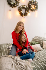 Cute mom and daughter are sitting near the christmas tree among the festive decorations 