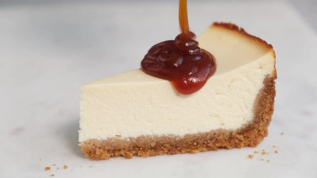 Caramel sauce pouring on slice of cheesecake on white marble background, closeup view