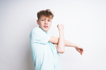 A caucasian teenage boy stretching his arm on a white backgorund