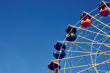 Ferris wheel against the blue sky. Multi-colored booths of the attraction against a clear sky.