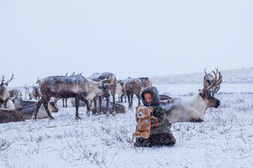 The Yamal Peninsula. Reindeer with a young reindeer herder. Happy boy on reindeer herder pasture playing with a toys in winter © evgenii