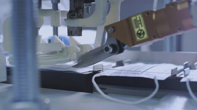 Production of medical protective face masks for air filtration. Coronavirus protection machine, covid-19. Steel scissors cut the thread to attach the mask to the face. Macro production line, conveyor.