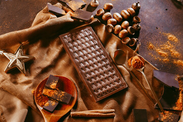 chocolate bar with orange. spices are sprinkled on the surface, orange citron and pieces of dark chocolate on a dark brown background.
