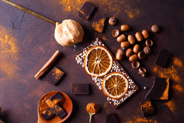 chocolate bar with orange. spices are sprinkled on the surface, orange citron and pieces of dark chocolate on a dark brown background.