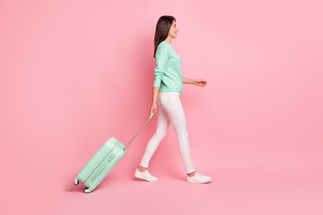 Full length body size profile side view of pretty cheerful girl traveler going with valise isolated on pink pastel color background