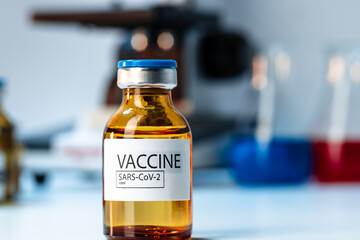 Vial of Covid-19 vaccine next to a microscope
