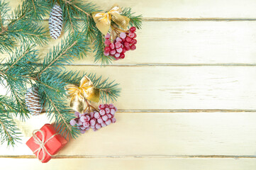 Christmas decoration, spruce branches with a bunch of red berries and yellow bows, Christmas cones and a red gift box on a gold wooden background close-up