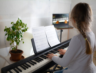 Girl learning to play the piano in distance learning via laptop over the Internet
