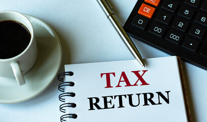 TAX RETURN - words written in a notebook against the background of a calculator and a cup of coffee