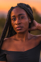 Lifestyle, Latina girl with black skin with beautiful long braids in her hair, wearing a tight black short dress. Portrait of the young man on top of the mountain in a beautiful summer sunset