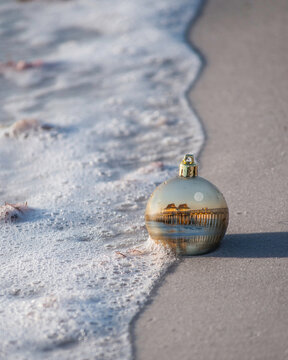 Christmas ball decoration in the sand on tropical shore.
