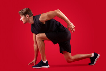 Side view of fit young sportsman standing on start over red studio background