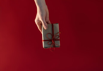 Top view of female hands holding present or gift box package in the palms isolated over flat lay red background.