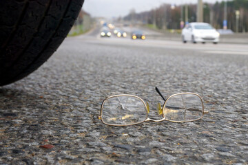  Spectacles with broken glass lie on the road under the wheel of a car. The concept of road...