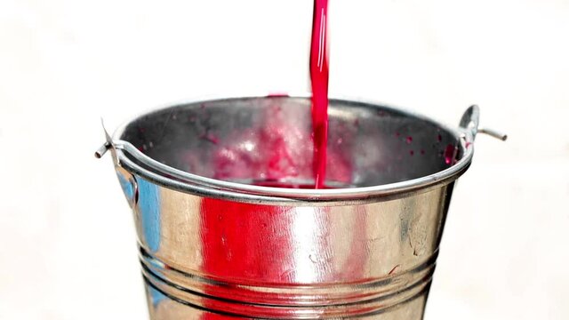 The red liquid is poured into a steel bucket and drip down, isolated on white background, slow motion.