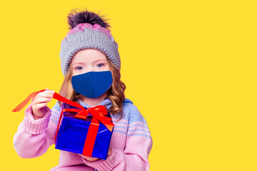 Beautiful little girl in the winter warm hat and scarf and medical mask stylish fashion child look in winter new year time