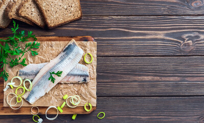 Herring fillet with parsley and onions on a cutting board, top view, dark wooden background. Traditional Norwegian or Danish smorrebrod ingredients. Herring sandwich, healthy food concept.