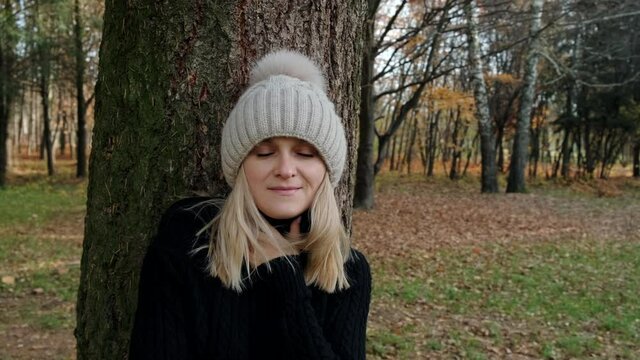 Portrait of a young blonde woman, who stands near tree in the forest. Close-up, slow motion.