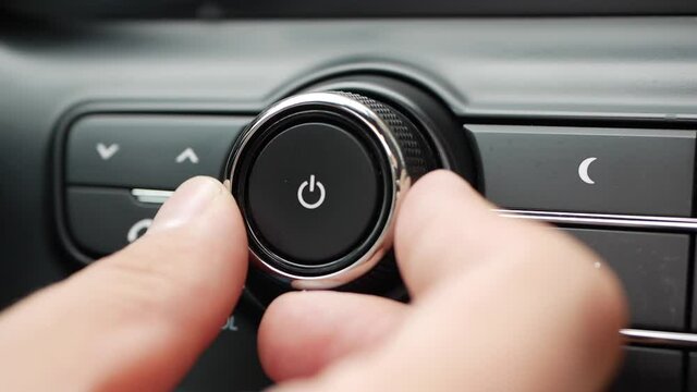 Male hand turning the volume of the radio inside car on travel day commuting in big city listening to the music on highway. Volume level adjusting on car audio system. Closeup