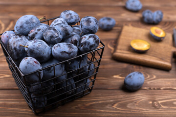 Lots of ripe juicy plums in a bowl on the brown wooden table.