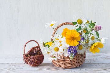 Fototapeta na wymiar Wicker basket with summer flowers bouquet on white paint wooden background. Greeting card