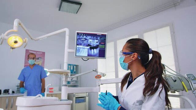 Dentist doctor and patient looking at digital teeh x-ray in dental office, person pov. Stomatology wearing protective face mask and gloves pointing at teeth radiography in stomatological clinic