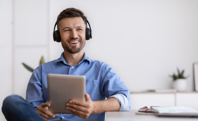 Handsome Freelancer Guy In Headphones Relaxing With Digital Tablet At Home Office