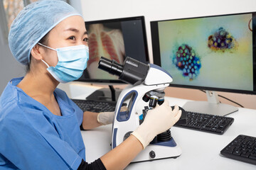 Femme médecin asiatique regarde au microscope des images médicales du covid-19 et de scanner des...