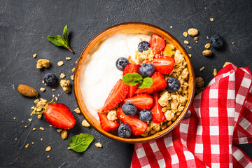 Yogurt granola with fresh berries on black stone table. Top view with copy space. Healthy food, snack or breakfast.