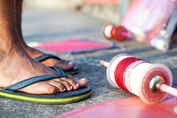 Young man with rubber slippers chappal with a charkhi fikri spool with dor thread with glass thread...